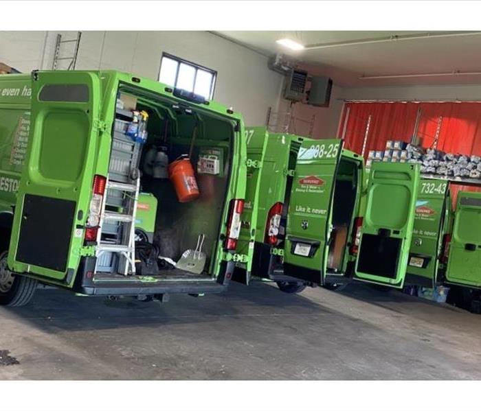 3 green SERVPRO vans sitting in a warehouse filled with equipment